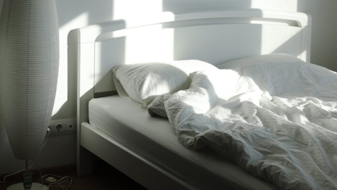 An empty bed and floor lamp in morning sunlight