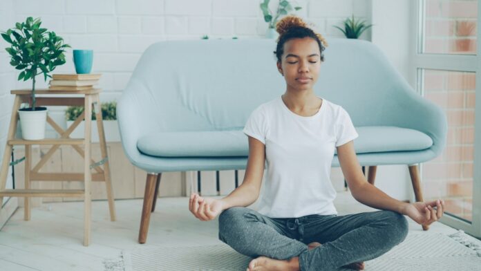 A young woman sitting cross-legged meditating on the floor at home